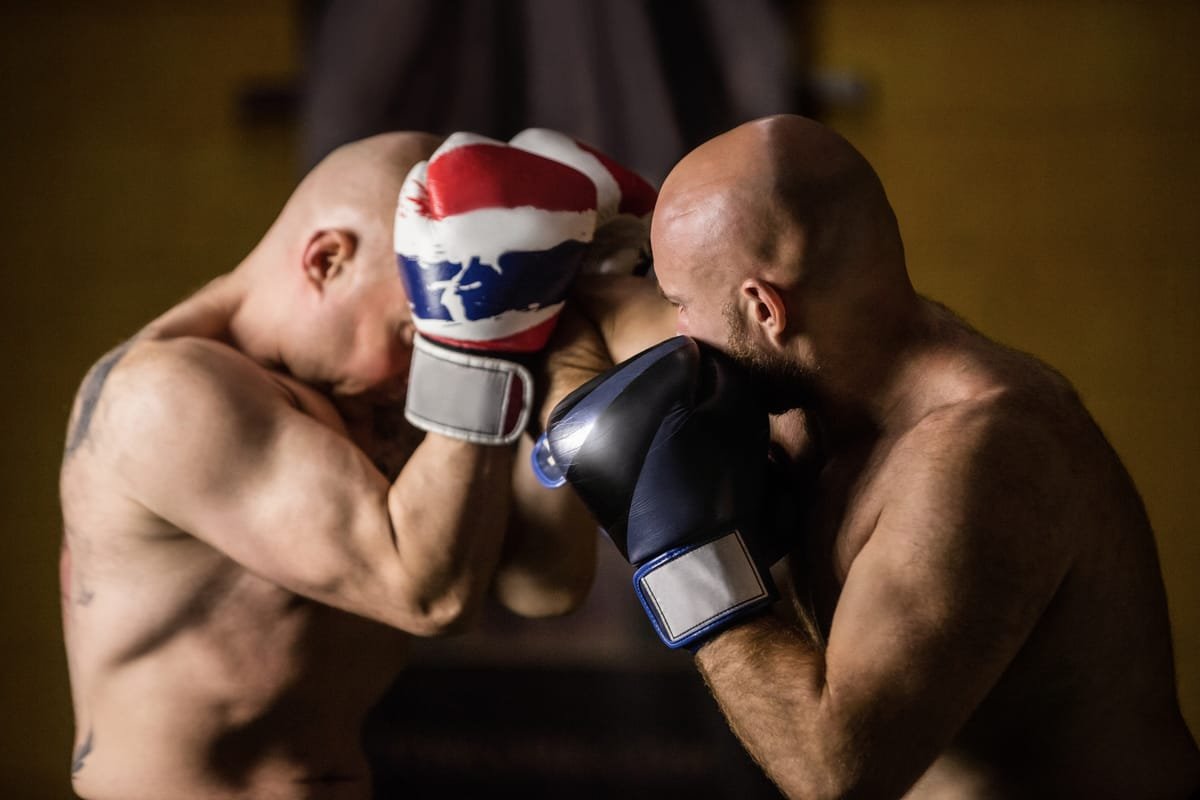 Dois lutadores sem camisa trocam golpes com luvas de muay thai em treino de sparring